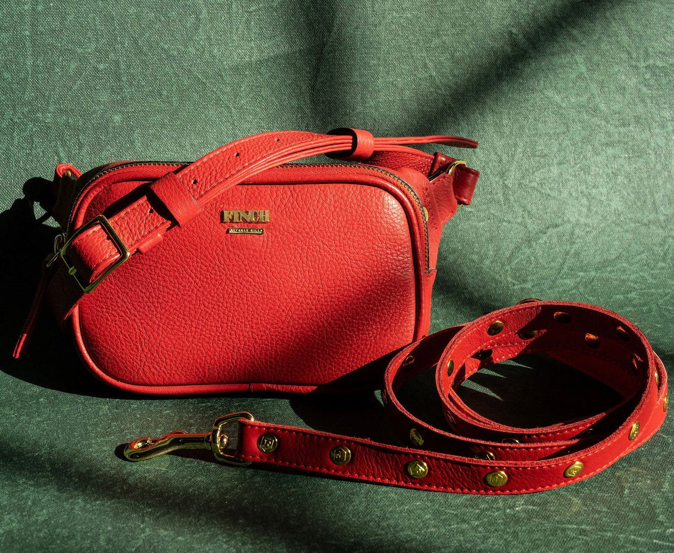 Red leather beltbag with red studded pet leash on a dark green fabric background